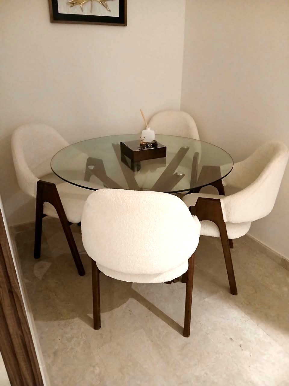 Table ronde en verre sur piètement en bois foncé, entourée de quatre chaises garnies de bouclette blanche