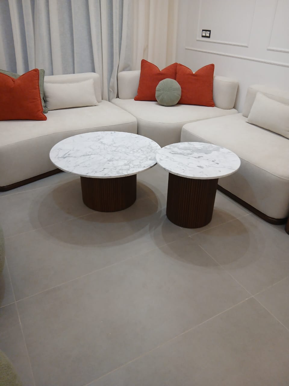 Deux tables basses rondes à plateau en marbre blanc et pied cannelé en bois foncé, devant un canapé d'angle